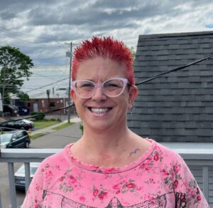 Woman in a pink flowered shirt, glasses, and red hair